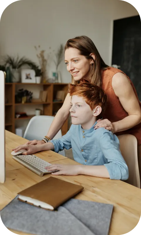 An adult helping a boy at a computer