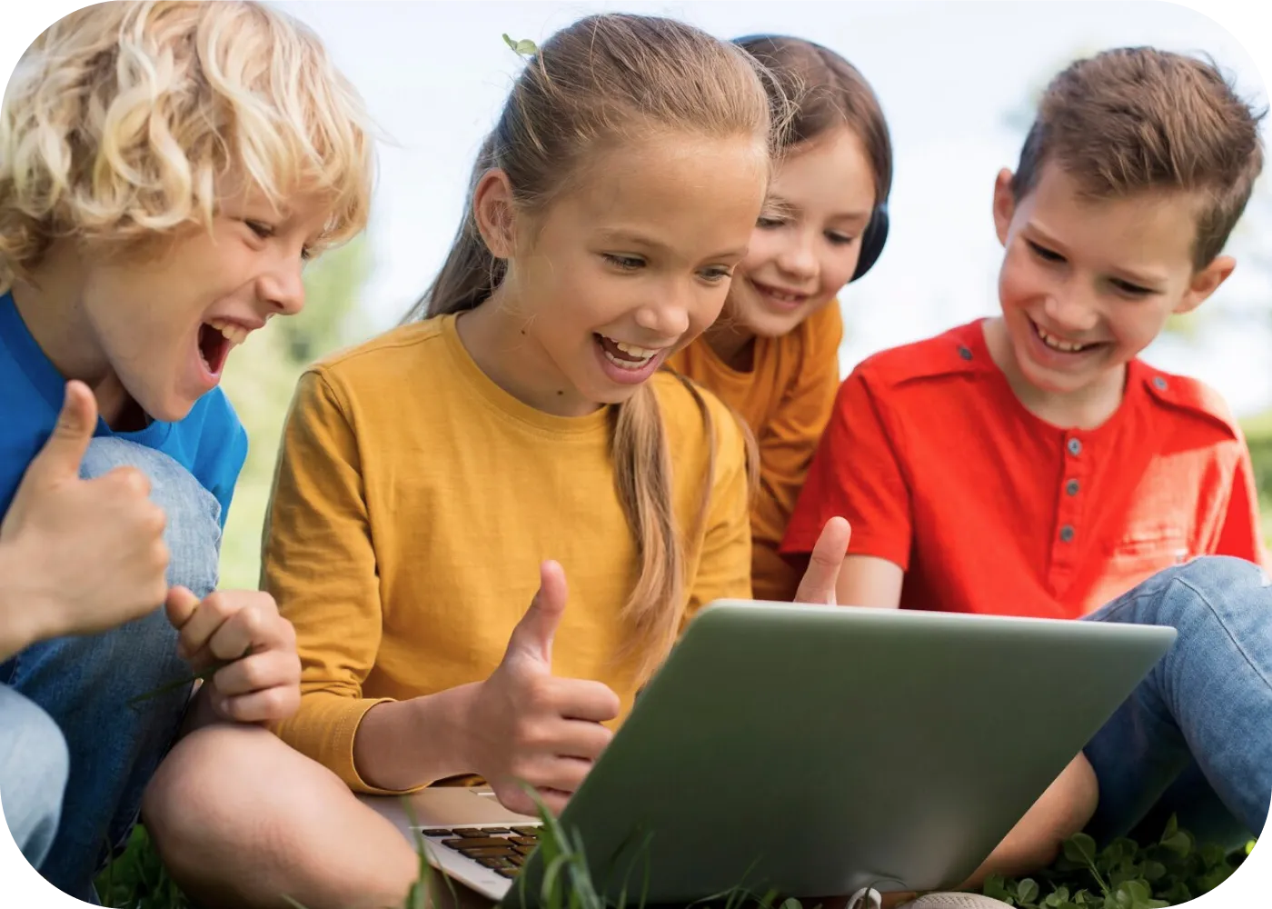 Four children sitting on the grass look at a laptop and give a thumbs up