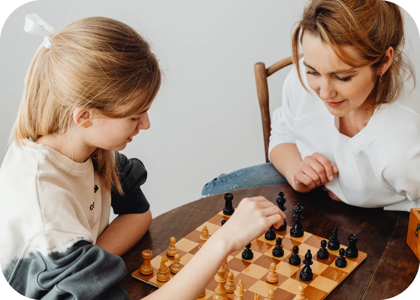 A girl and a woman playing chess at a wooden table